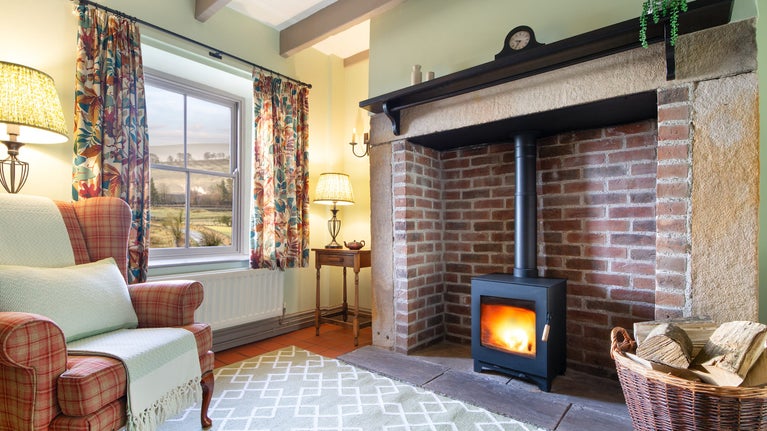 A corner of the sitting room at Peel Cottage, showing an armchair, the woodburner and views of the surrounding countryside, Northumberland